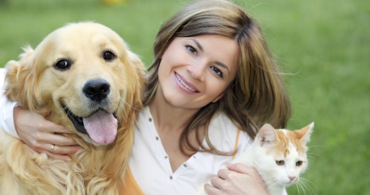 An image showing a happy and smiling girl with her pet dog and cat.