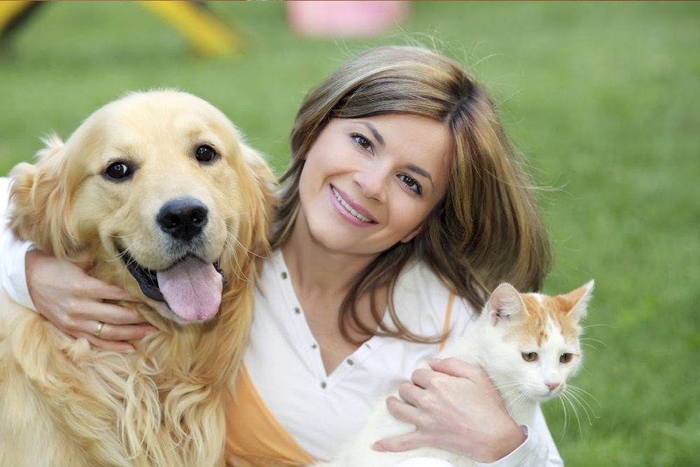An image showing a happy and smiling girl with her pet dog and cat.